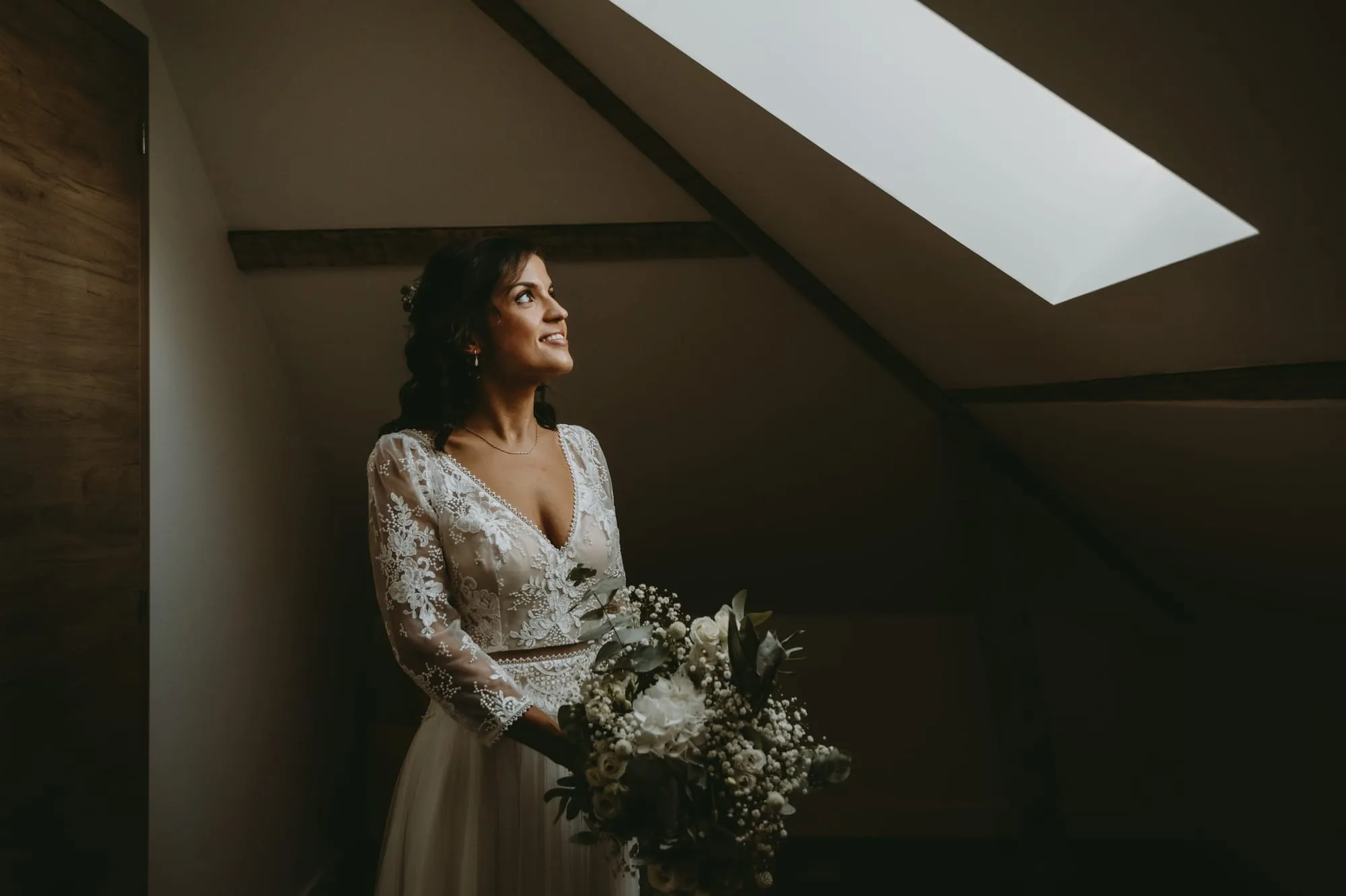 Mariée regardant la lumière d'une lucarne, son bouquet à la main