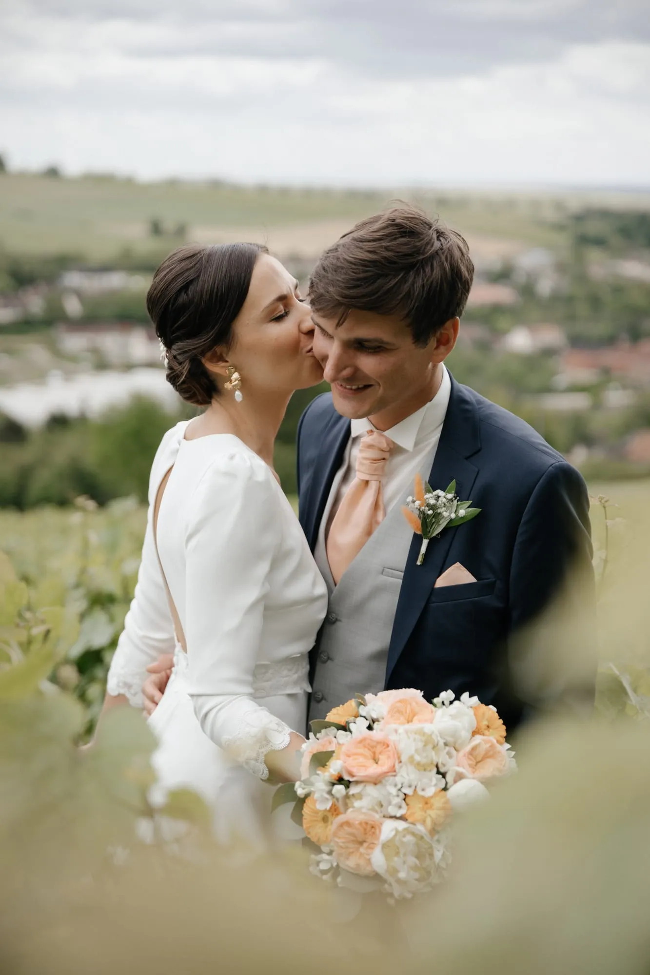Mariée embrassant la joue du marié, bouquet de fleurs au premier plan