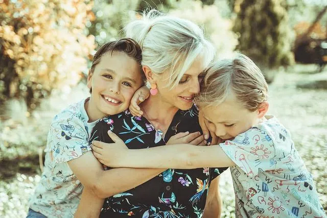 Mère riant, enlacée par ses deux fils, en extérieur