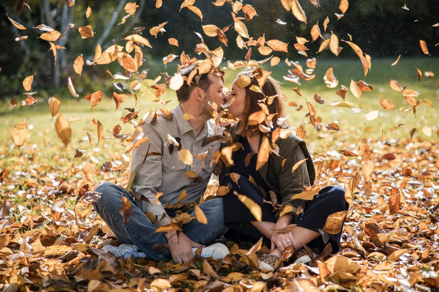 Couple s'embrassant assis dans les feuilles d'automne qui tombent