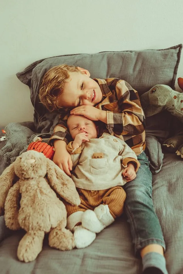 Grand frère câlinant son petit frère nouveau-né sur le canapé, entourés de peluches