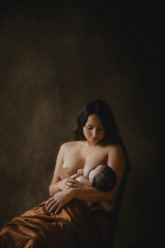 Mère assise allaitant son bébé, drap orangé, en studio