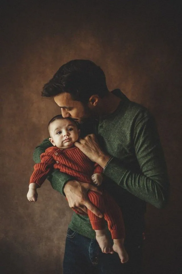Portrait de père embrassant le front de son bébé, pull vert