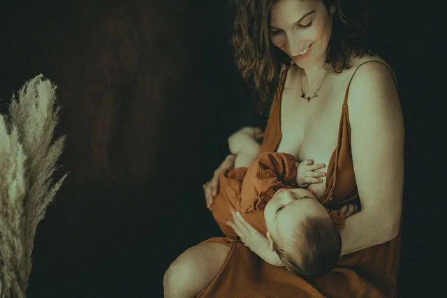 Mère souriante en robe rouille allaitant son bébé