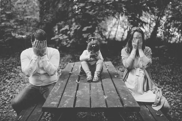 Famille en noir et blanc, les mains sur les yeux, sur une table de pique-nique en forêt
