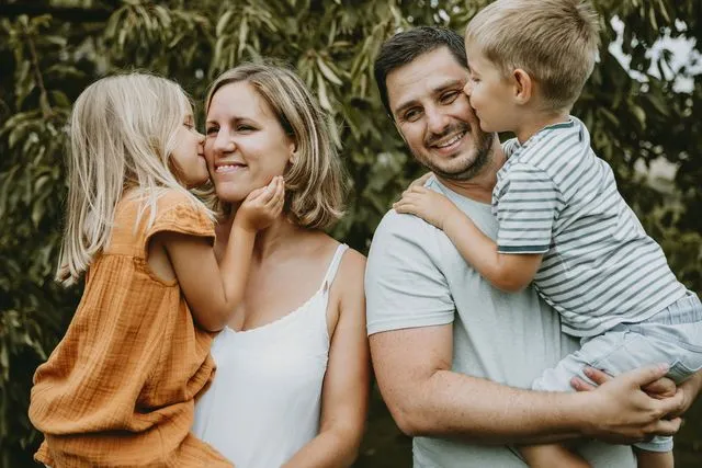 Famille de quatre, les enfants embrassant leurs parents sur la joue, en extérieur