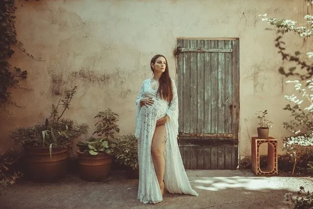 Femme enceinte en robe de dentelle blanche devant une porte en bois ancienne