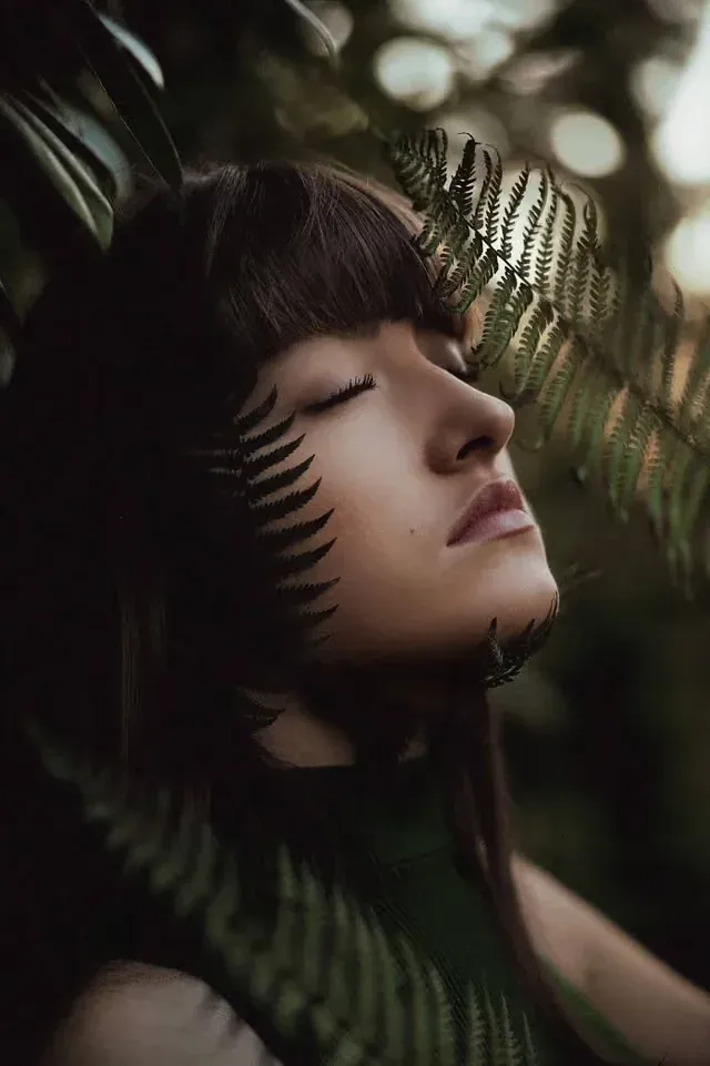 Portrait d’une jeune femme aux yeux fermés parmi les fougères