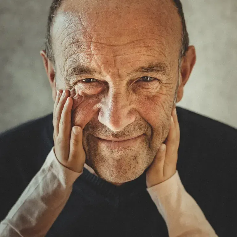 Portrait d’un homme souriant, les mains d’un enfant sur ses joues