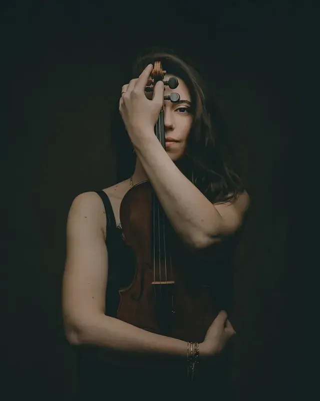 Portrait d’une violoniste, un œil caché derrière son violon